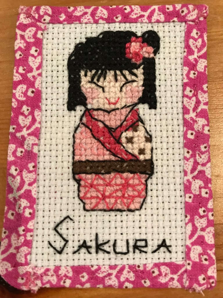 Cross Stitch image of a japanese woman in traditional kimono, with the title 'Sakura' and a pink border.