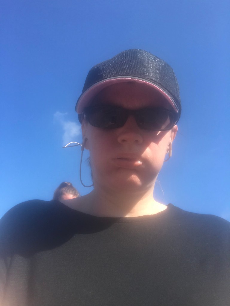 Image of Rebecca in a cap and sunglasses with an exhausted look on her face, with a bright blue sky in the background.